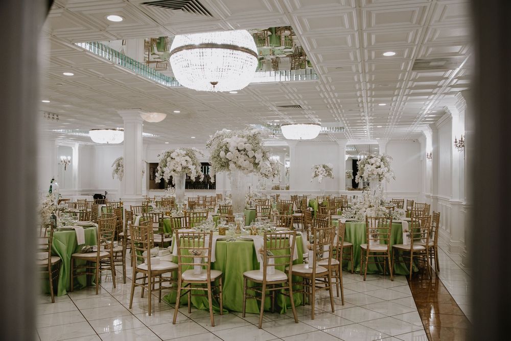 Elegant banquet hall with green tablecloths, gold chiavari chairs, floral centerpieces, and crystal chandeliers.