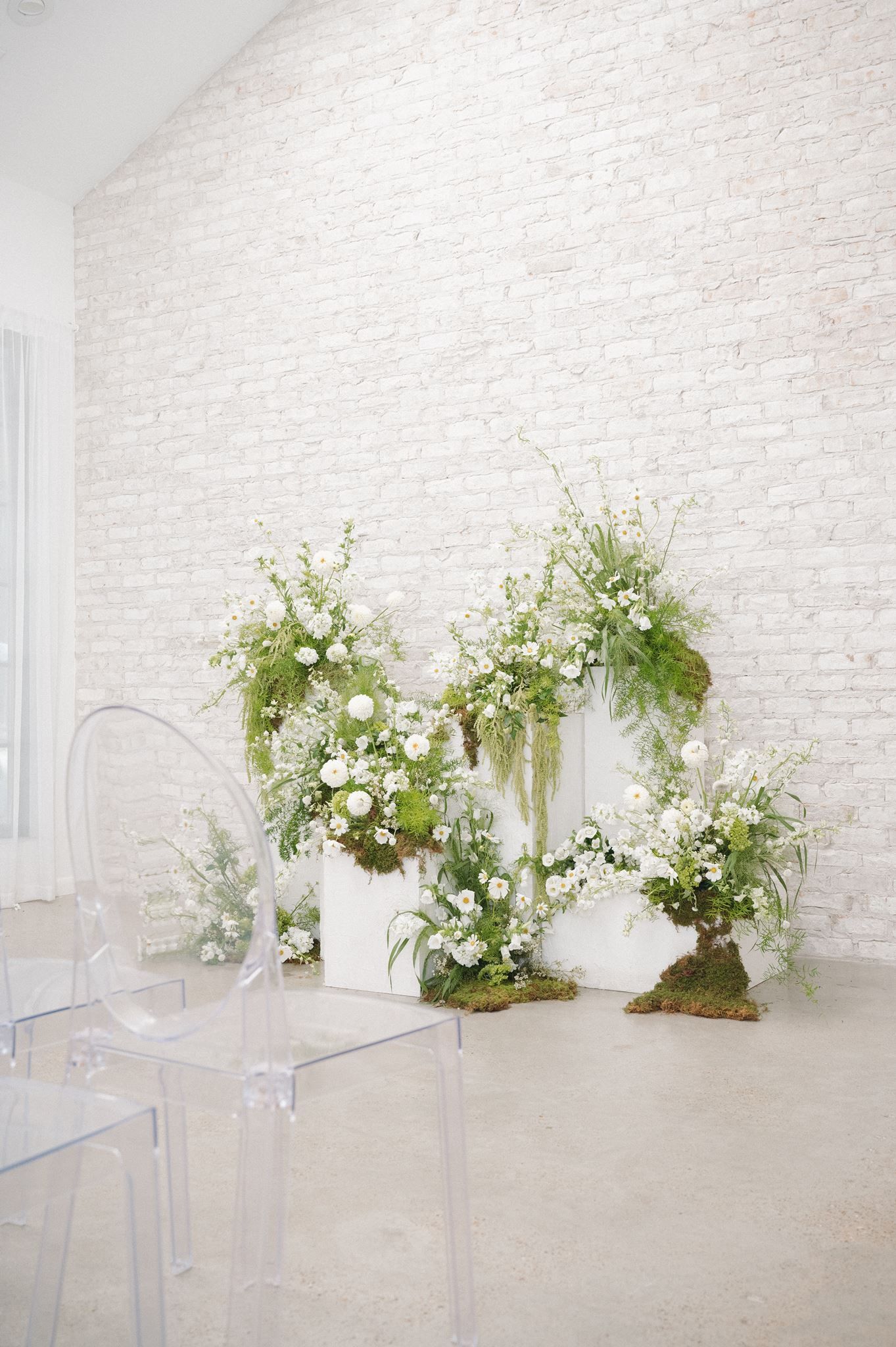 White floral arrangements with greenery and ferns displayed against a whitewashed brick wall at the Oak Atelier in Conroe, Texas.