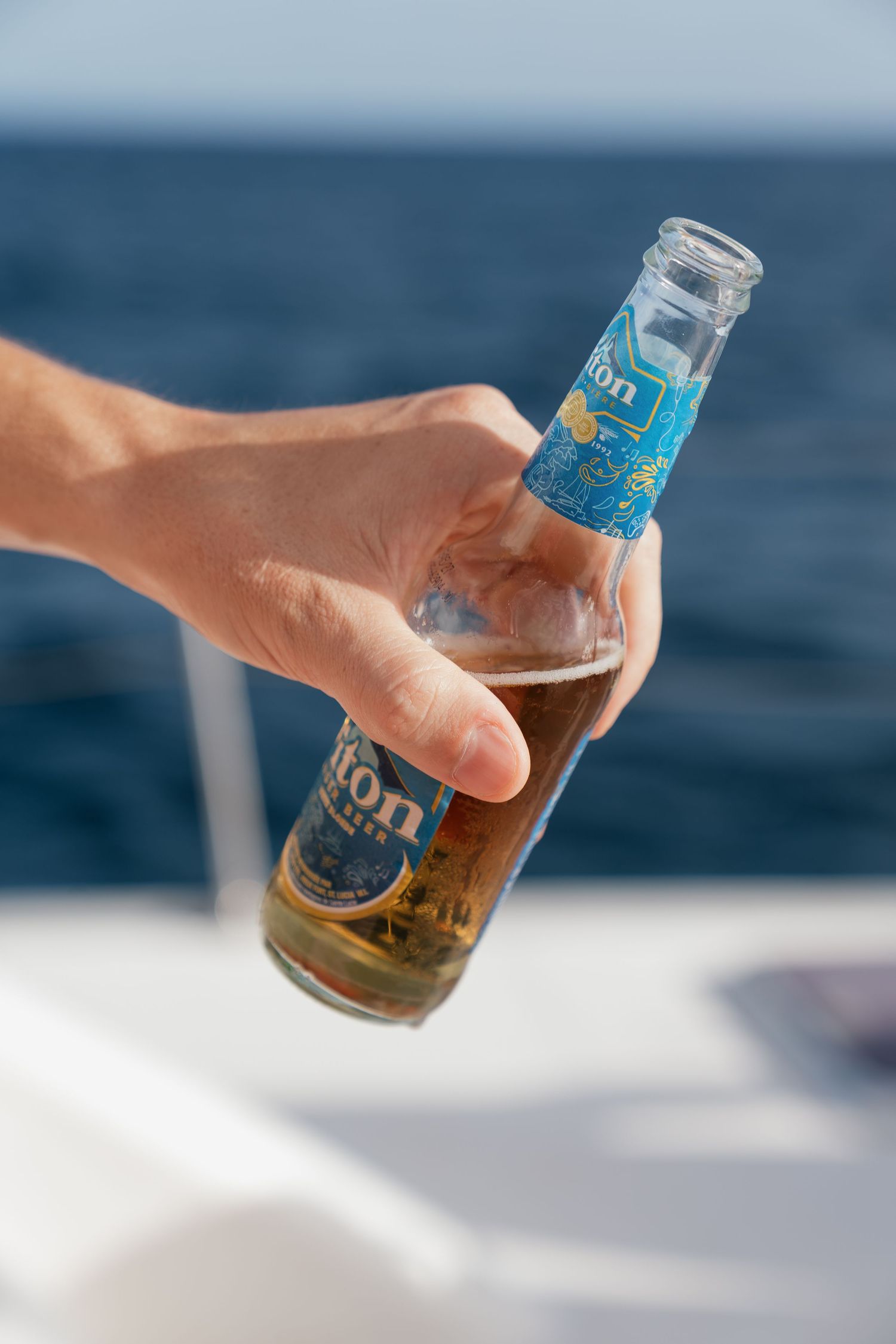 Hand holding a cold bottle of Leon beer on a boat with ocean in the background.