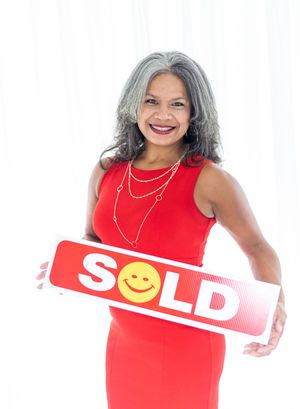 Smiling woman in red dress holding a SOLD real estate sign, perfect for property listings and agent marketing.