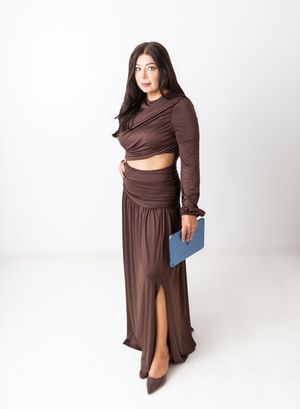 Woman in brown crop top and maxi skirt with slit, holding blue clutch, wearing brown heels.