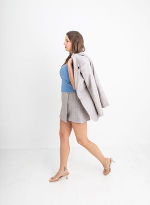 Woman walking in blue top, gray plaid mini skirt, and heels, carrying a matching blazer over her shoulder.
