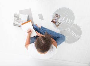 Overhead view of a person sitting on white floor reviewing real estate documents with sold property photos nearby.