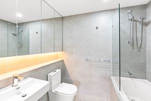 Contemporary bathroom with glass shower, bathtub, toilet and large vanity mirror with lighting.