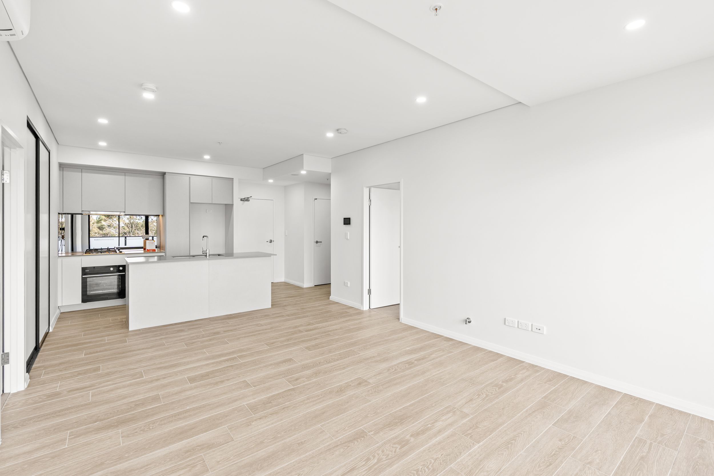 Modern open-plan kitchen with white island bench and light timber floors in new apartment.