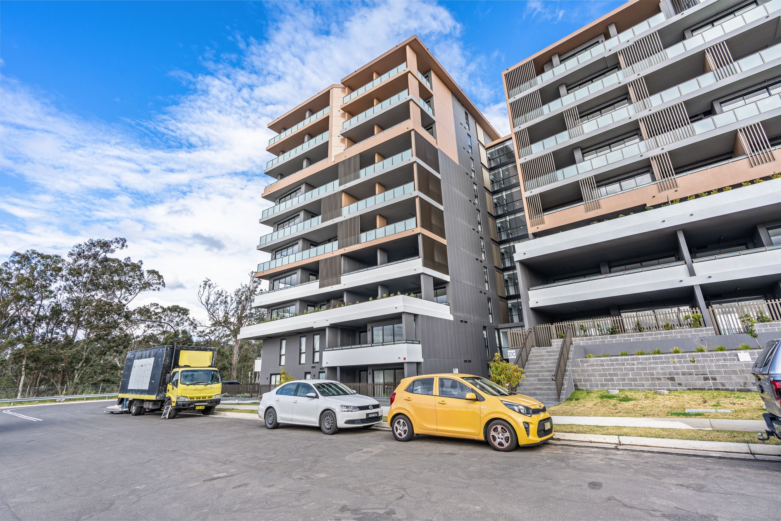 Modern multi-storey residential apartment building with balconies surrounded by trees.