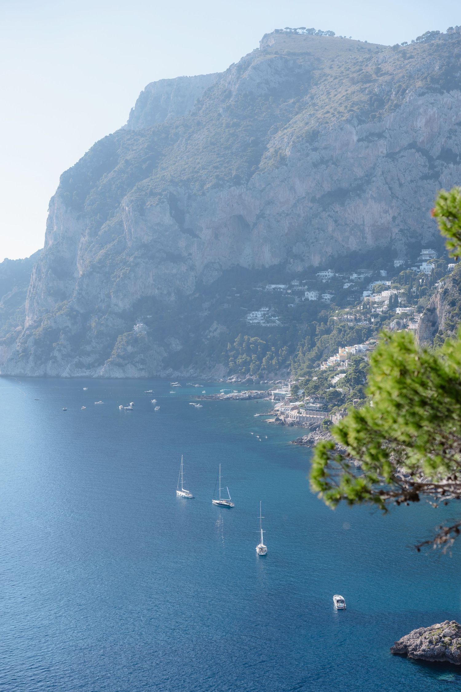 Scenic view of sailboats on blue Mediterranean waters with dramatic cliffs and coastal village, Capri, Italy.