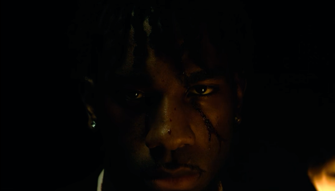Close-up portrait of a man with face paint in dramatic dark lighting with warm tones.