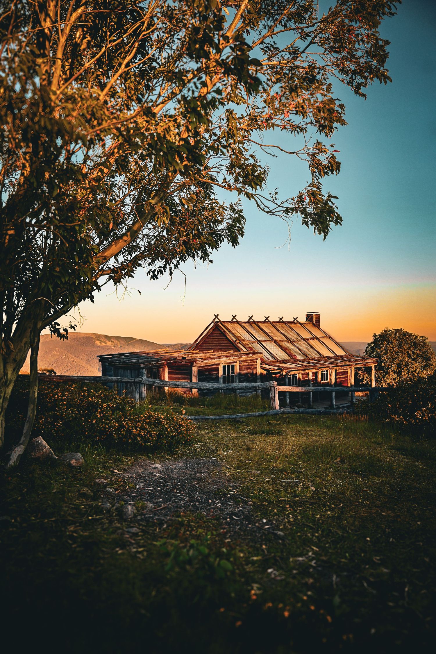 Rustic wooden hut at sunset with golden light, surrounded by trees and mountain views.