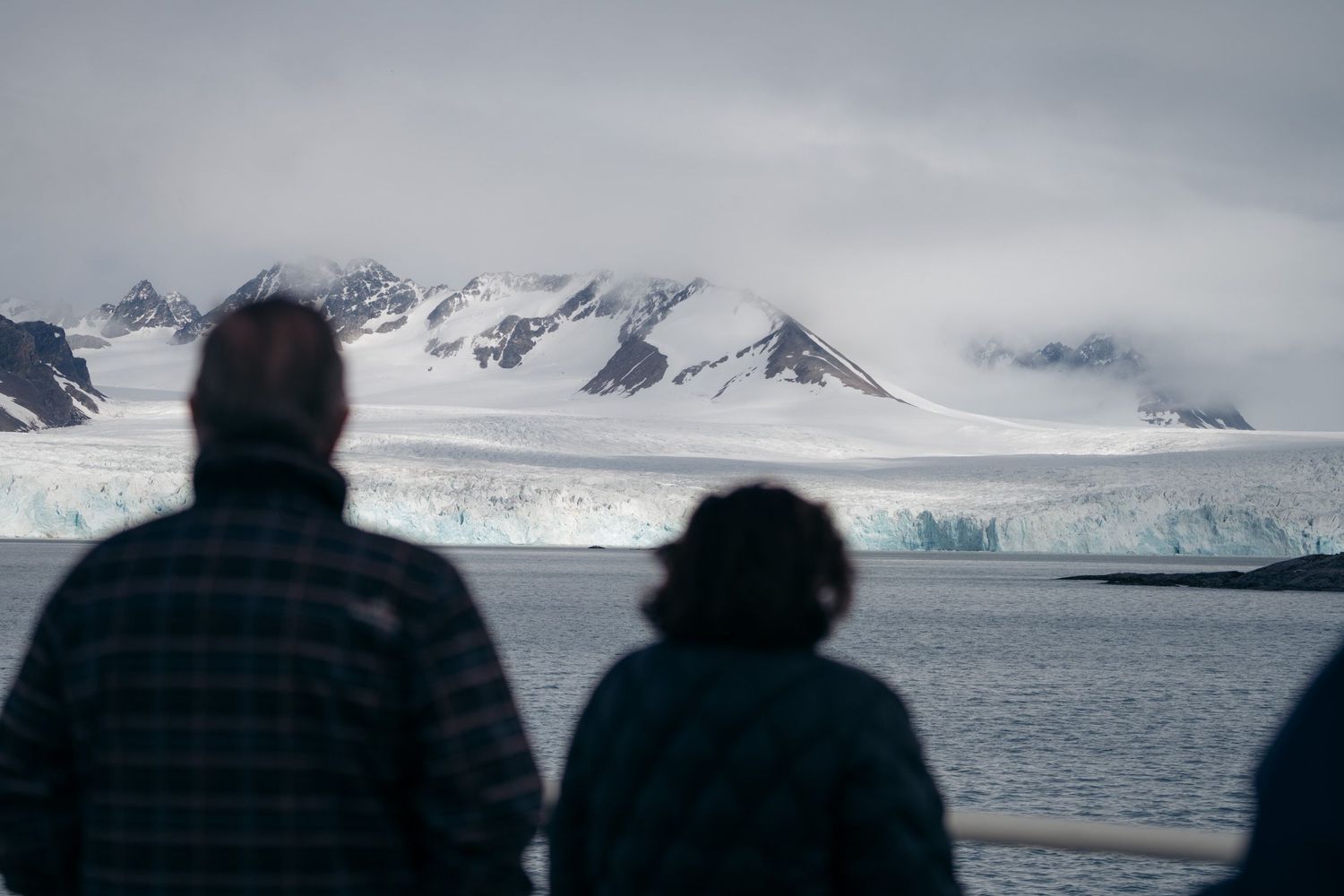 Deux passagers de dos observant un front glaciaire et ses montagnes enneigées