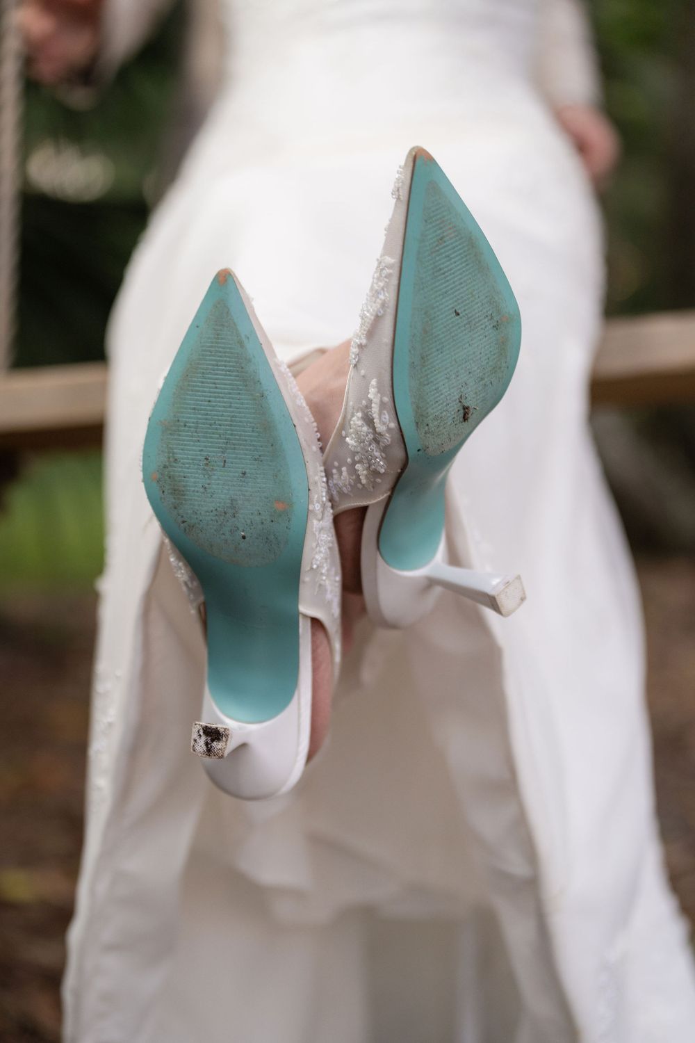 Bride showing worn teal-soled wedding shoes on a swing at White Trail Club, Jupiter, FL