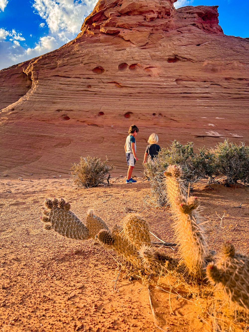 Two hikers exploring red sandstone rock formations with cactus in the Arizona desert landscape.