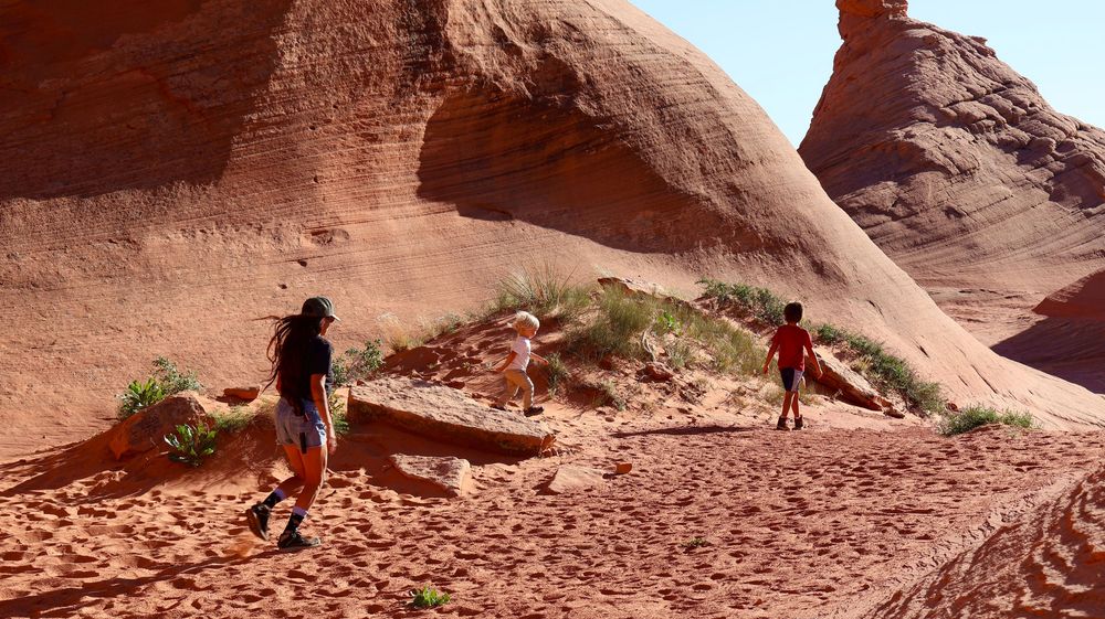 Family hiking through red rock canyon formations on a sunny desert trail.