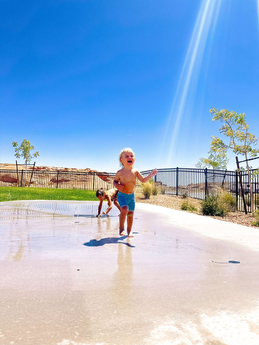 Happy toddler running through a splash pad water play area on a bright sunny day.