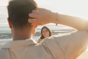 Couple sharing a romantic moment on a sunny beach at golden hour, woman smiling joyfully at camera.