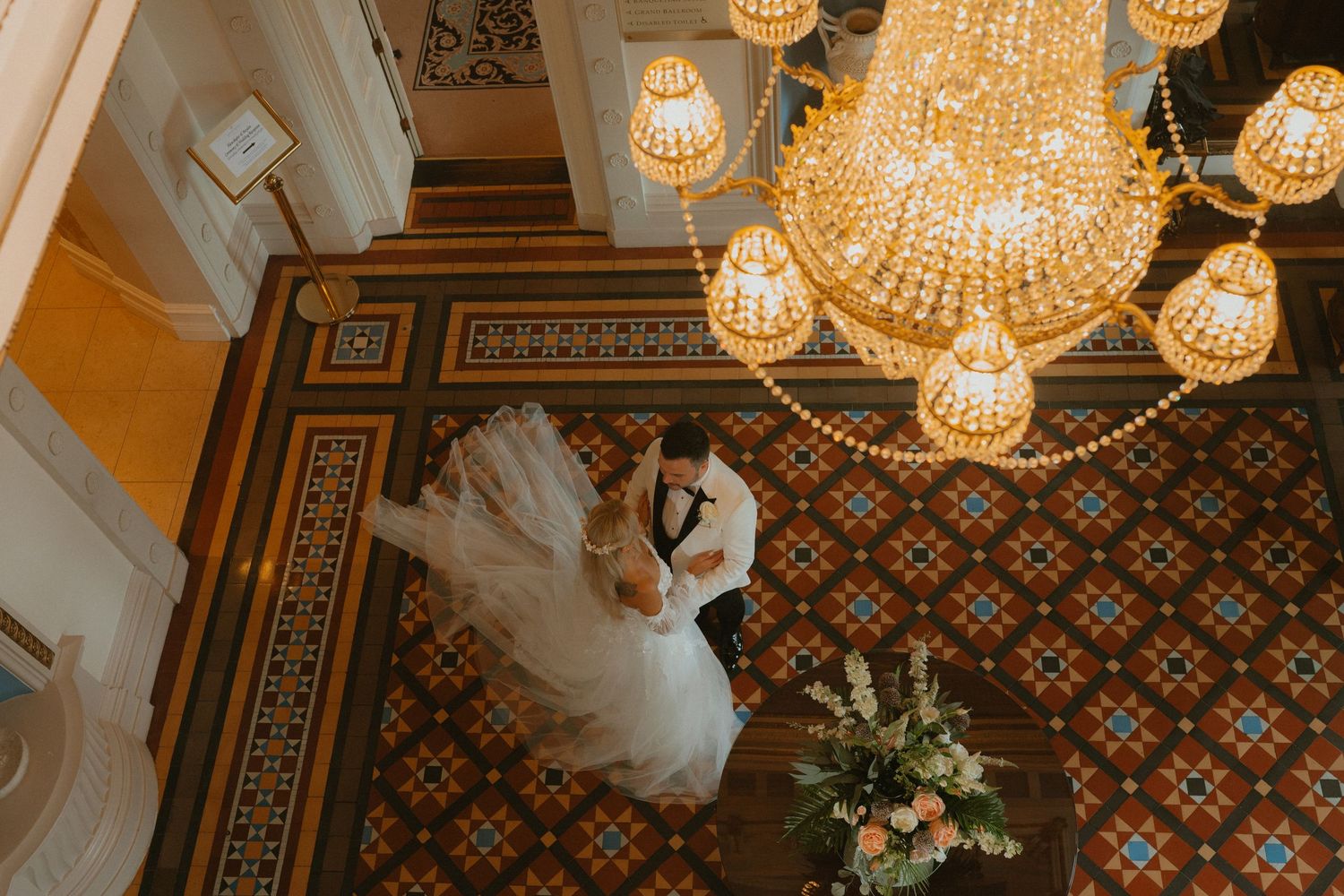 Aerial view of bride and groom sharing a romantic moment under an ornate chandelier at the Manor House, Co. Fermanagh