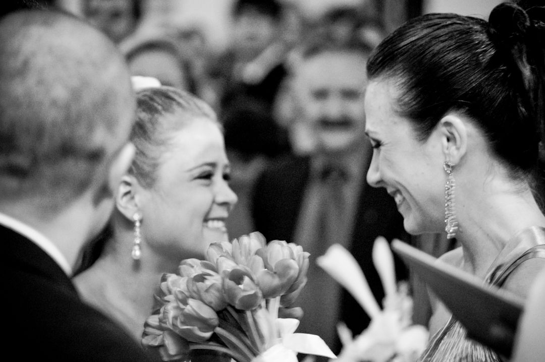 Two women smiling and exchanging flowers at a formal event in black and white photo.