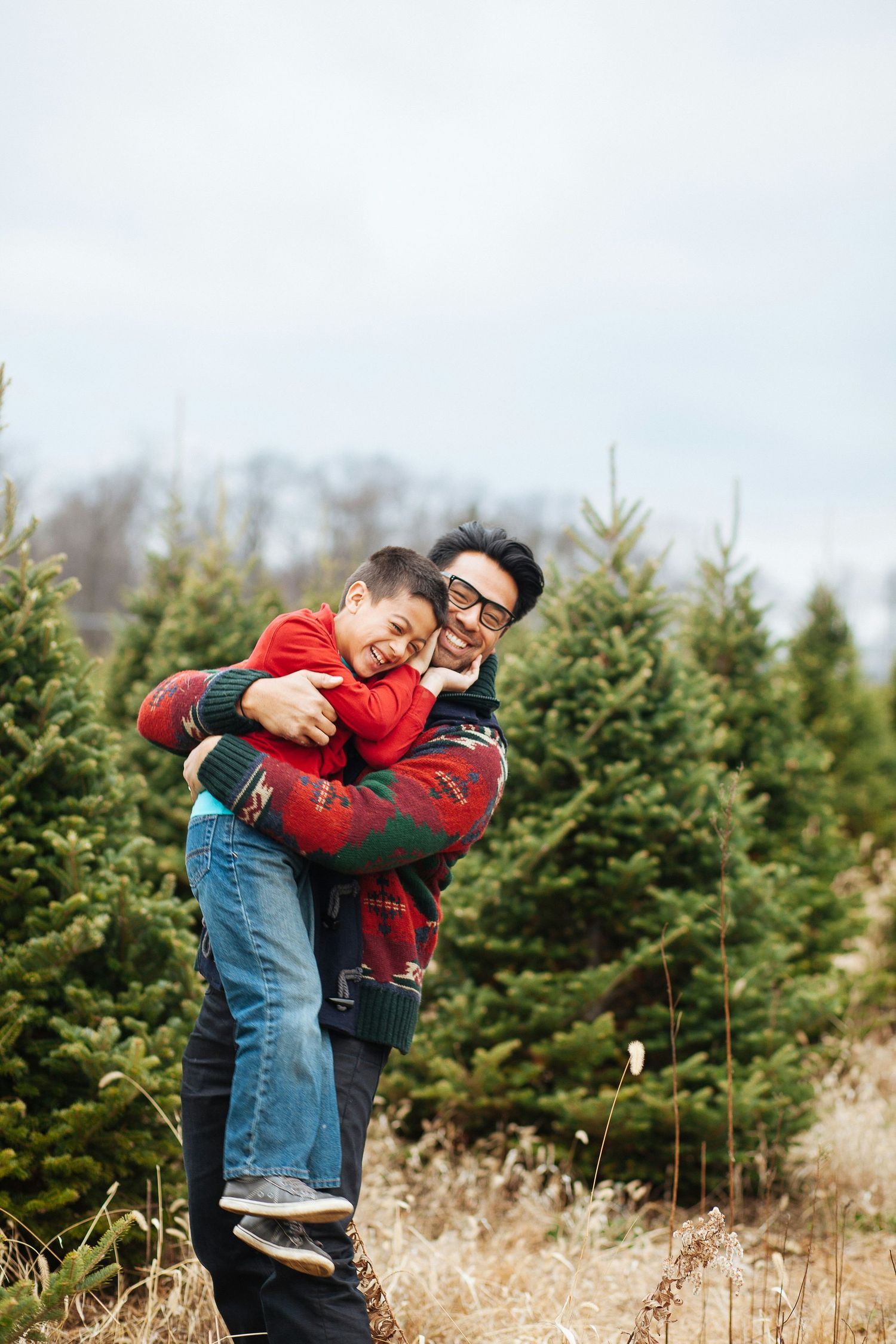 Father and son hugging and laughing together at a Christmas tree farm in winter.