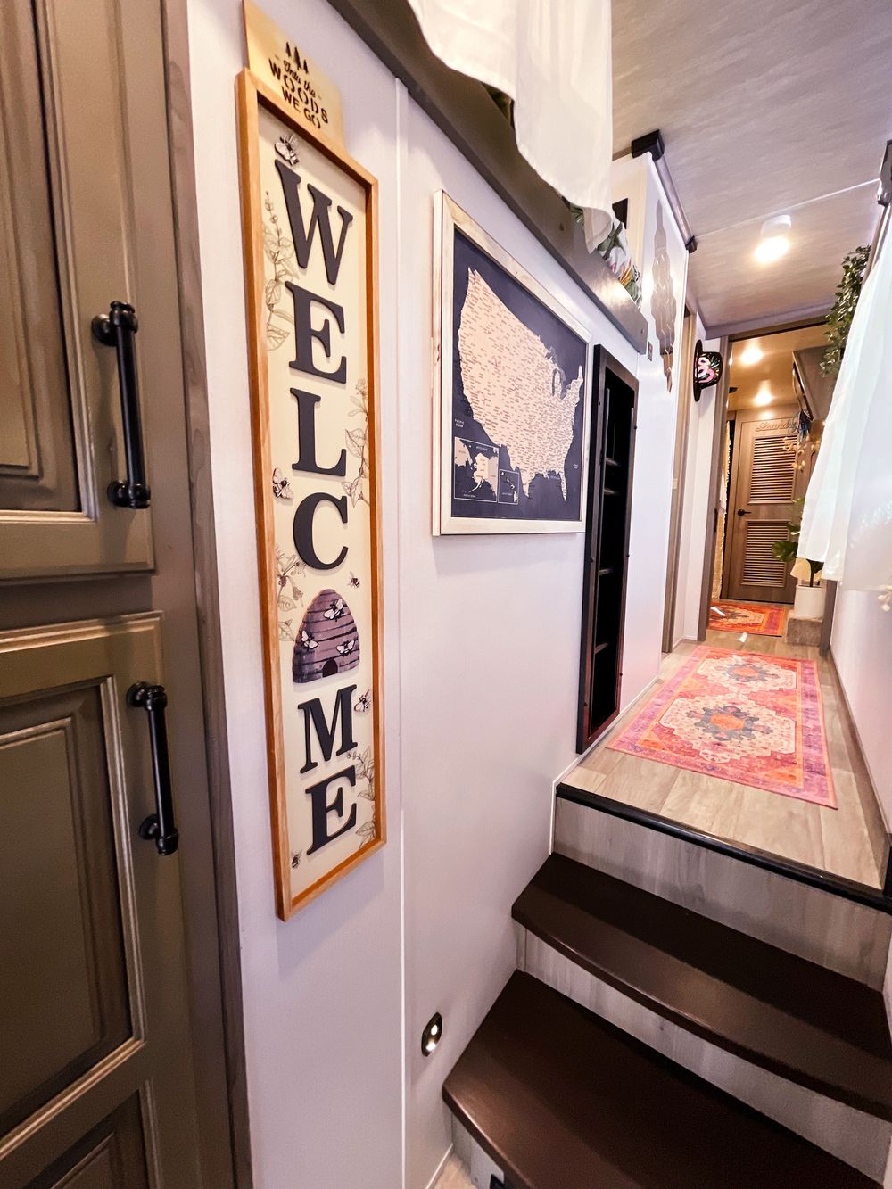 Welcoming RV entryway with vertical WELCOME sign, US map wall art, staircase, and decorative runner rug.