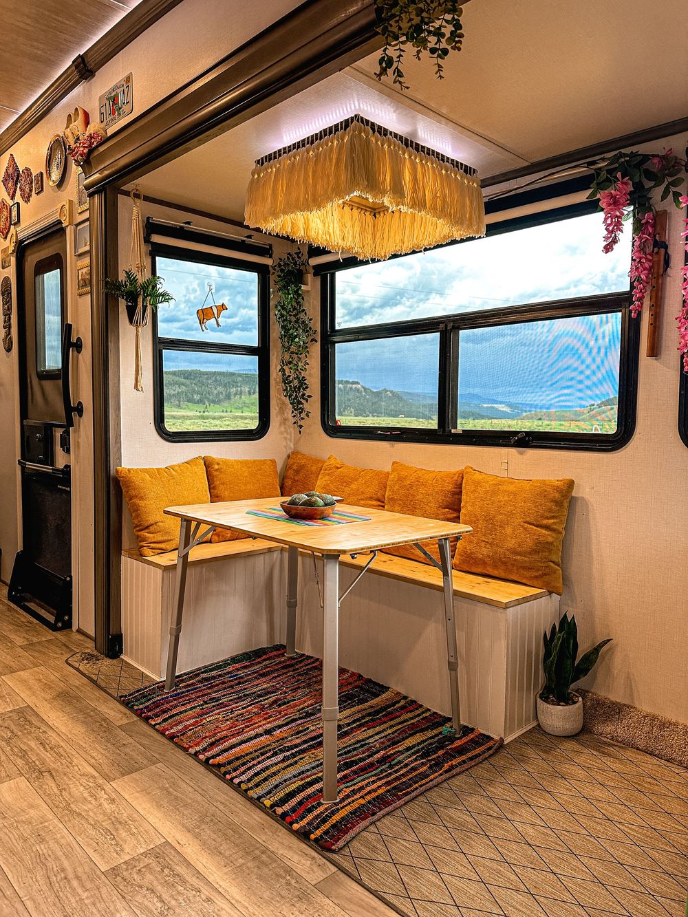 Boho RV dining nook with mustard cushions, fringe chandelier, and scenic view.