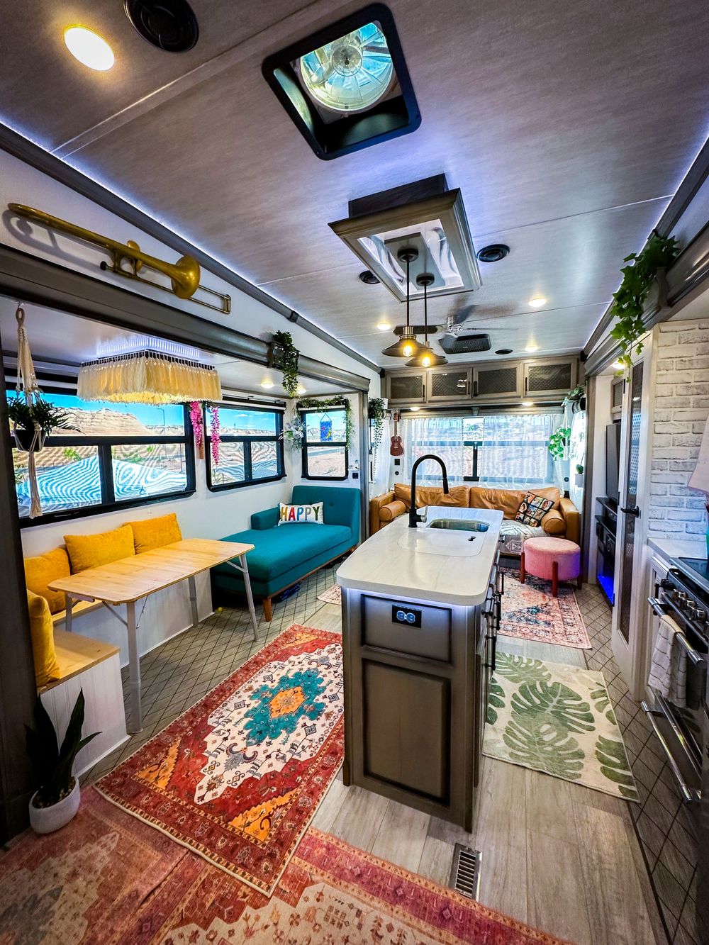 Colorful bohemian RV interior with fringe chandelier, kitchen island, and layered rugs.