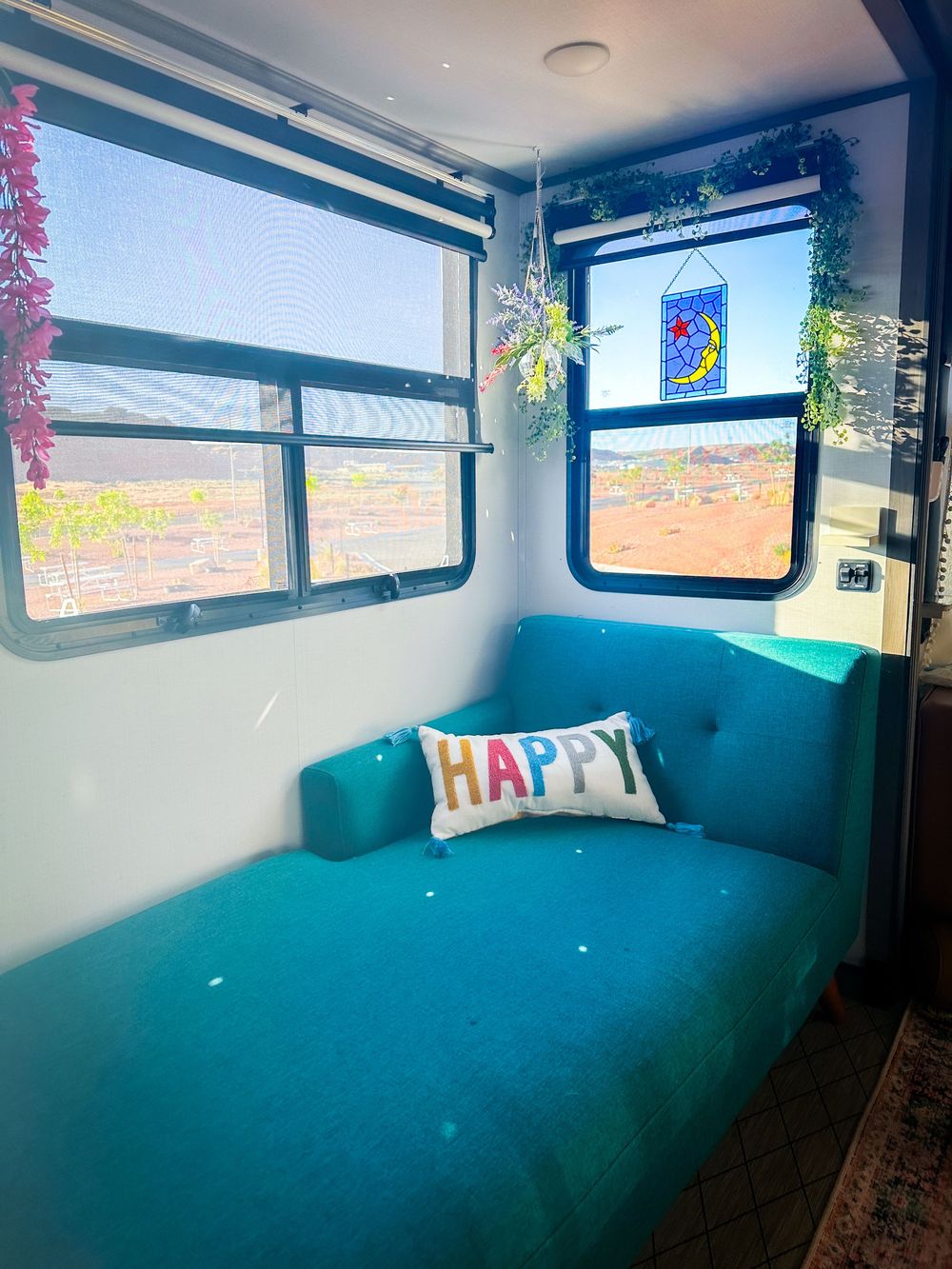 Bright RV lounge area with teal sofa, stained glass decor, and HAPPY pillow.