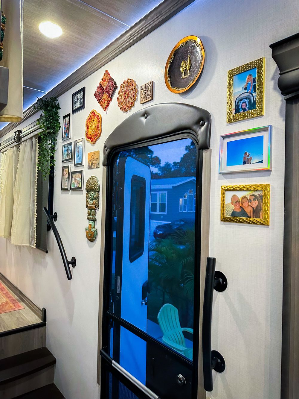 Eclectic RV entryway wall decorated with framed family photos, colorful art pieces, and a glass screen door.