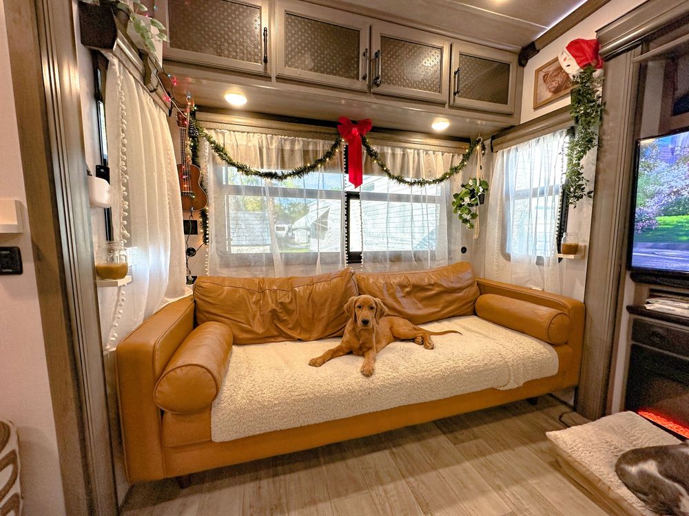 A golden dog resting on a tan leather sofa inside a holiday-decorated RV with Christmas garland and red stockings.