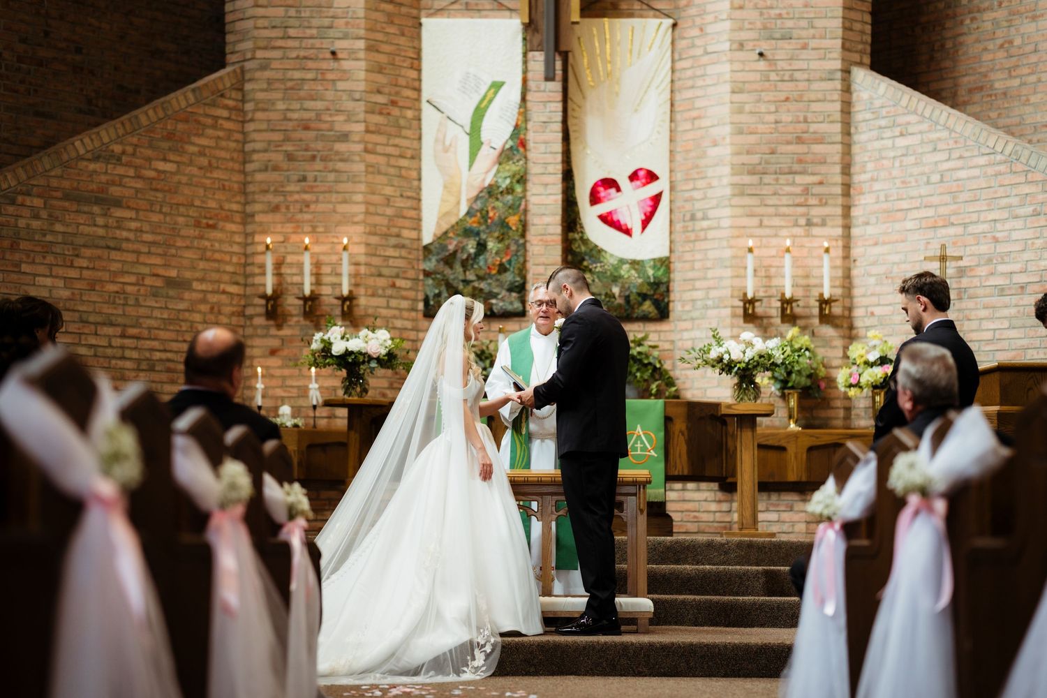 Bride and groom exchanging vows at a church altar during a traditional wedding ceremony with floral decorations.