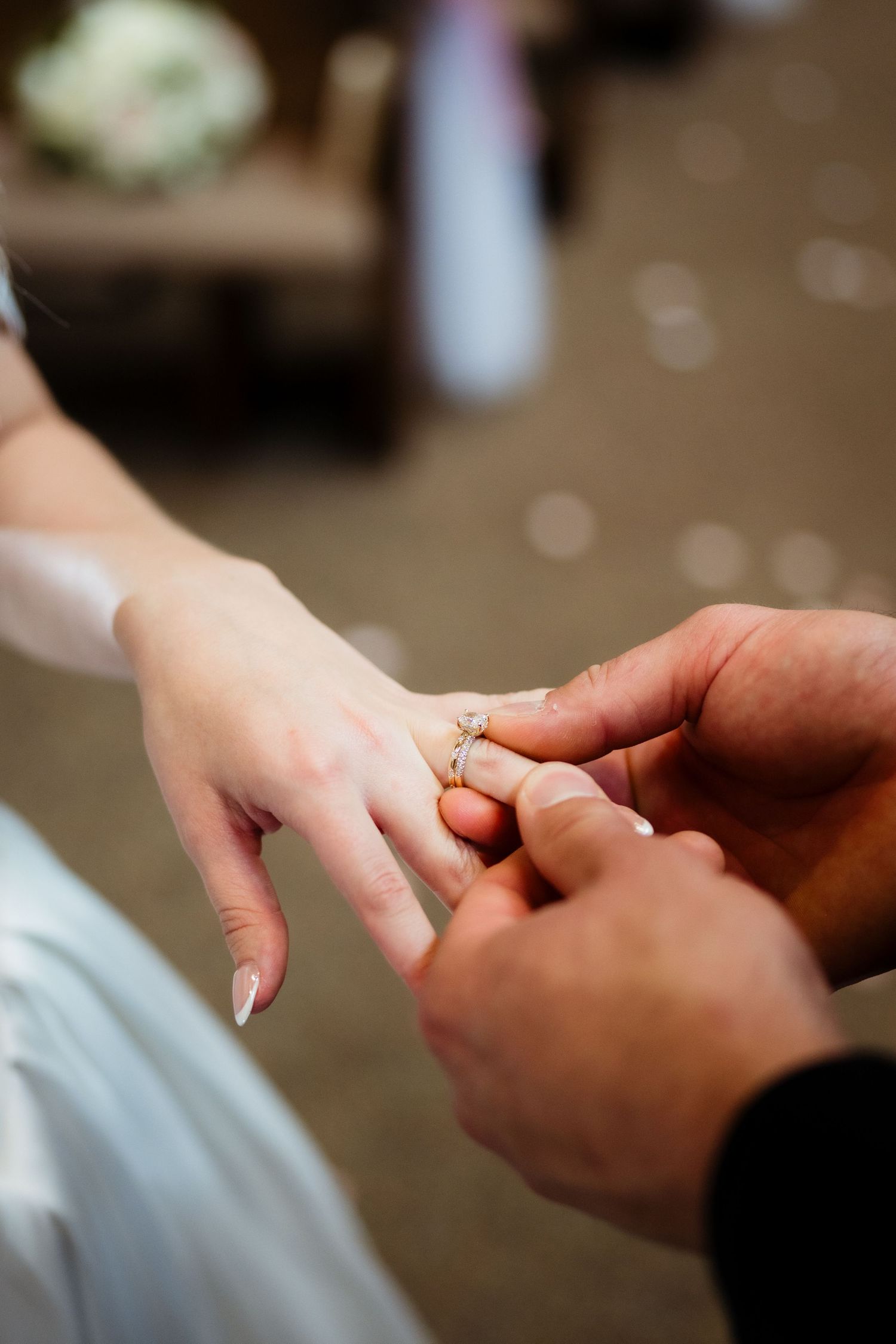 Groom placing a diamond engagement ring on bride's finger during wedding ceremony.