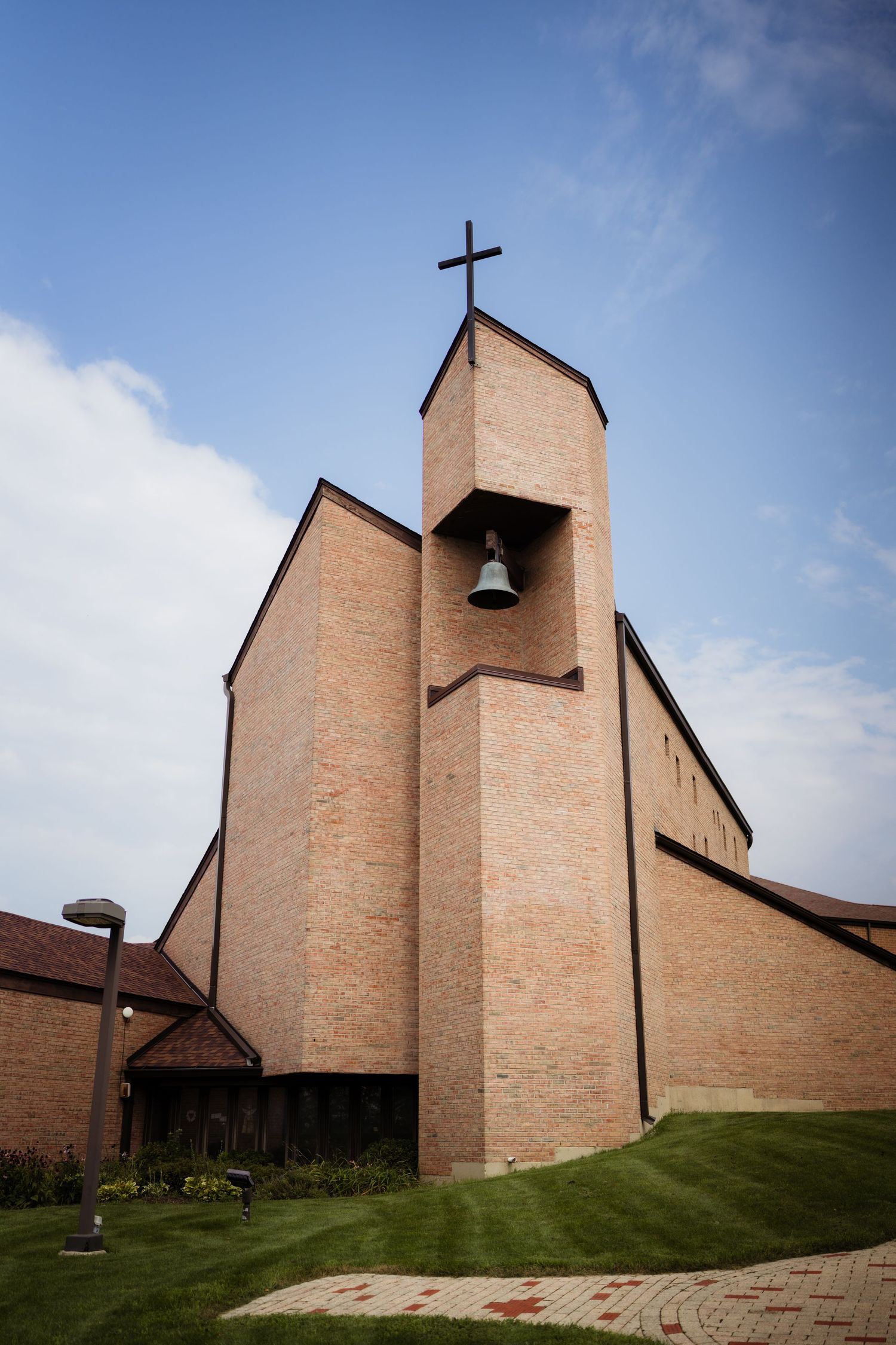 Modern brick church with bell tower topped by a cross against a blue sky, surrounded by green lawn.