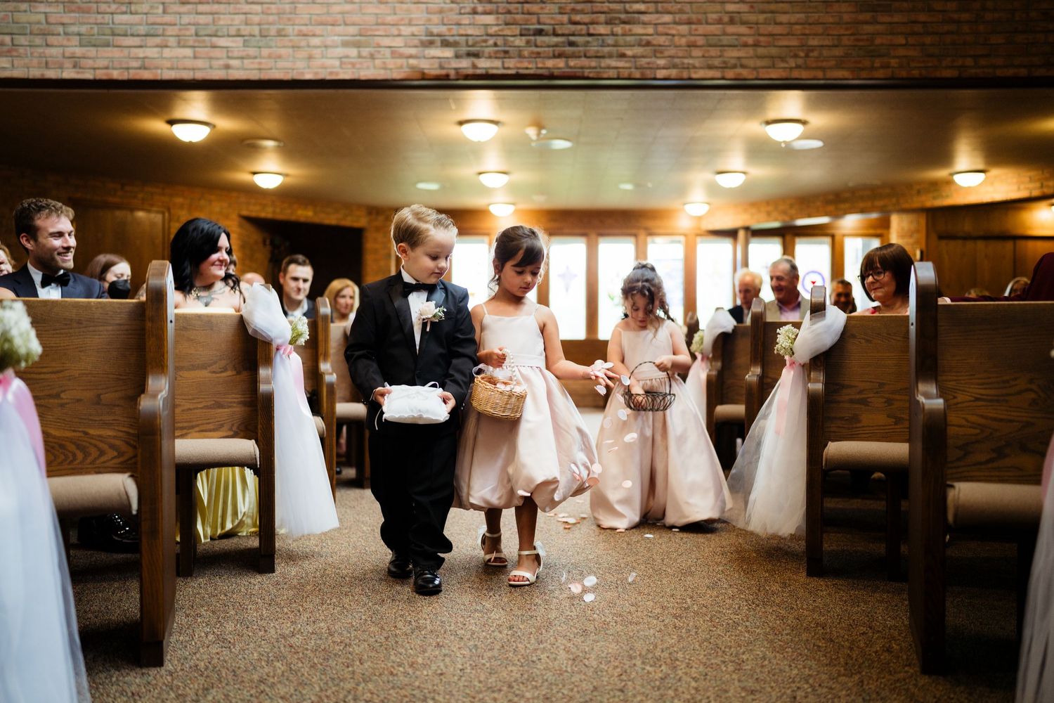 Flower girls and ring bearer walking down church aisle during wedding ceremony procession.