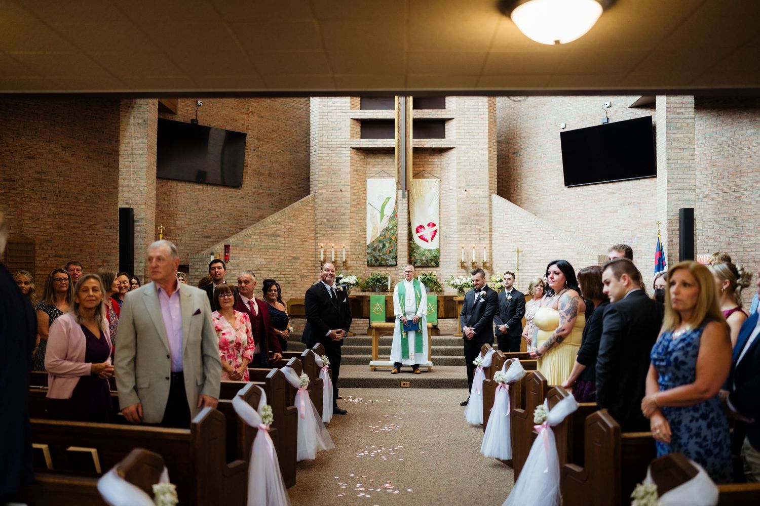 Wedding ceremony in a church with guests seated in pews as the bride walks down the aisle toward the altar.