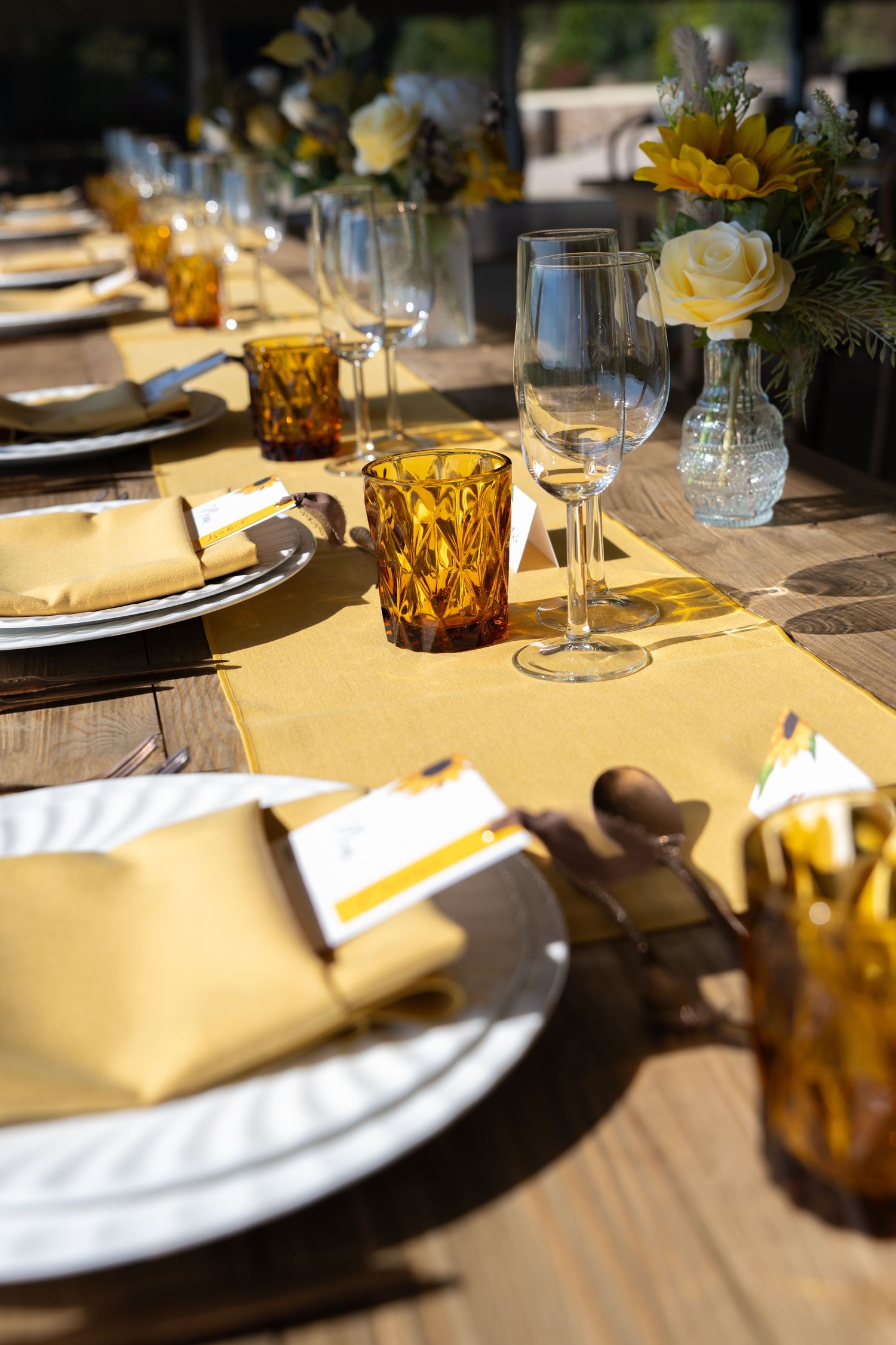 Elegant wedding reception table set with yellow napkins, amber glassware, and sunflower centerpieces.