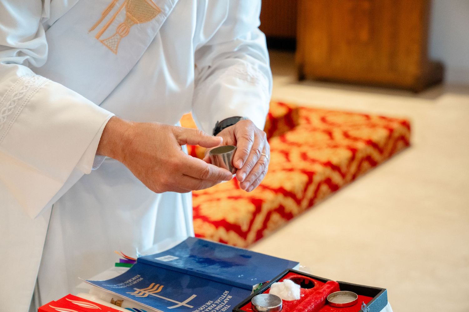 Priest in white vestments preparing communion elements at an altar with religious books and sacramental vessels.