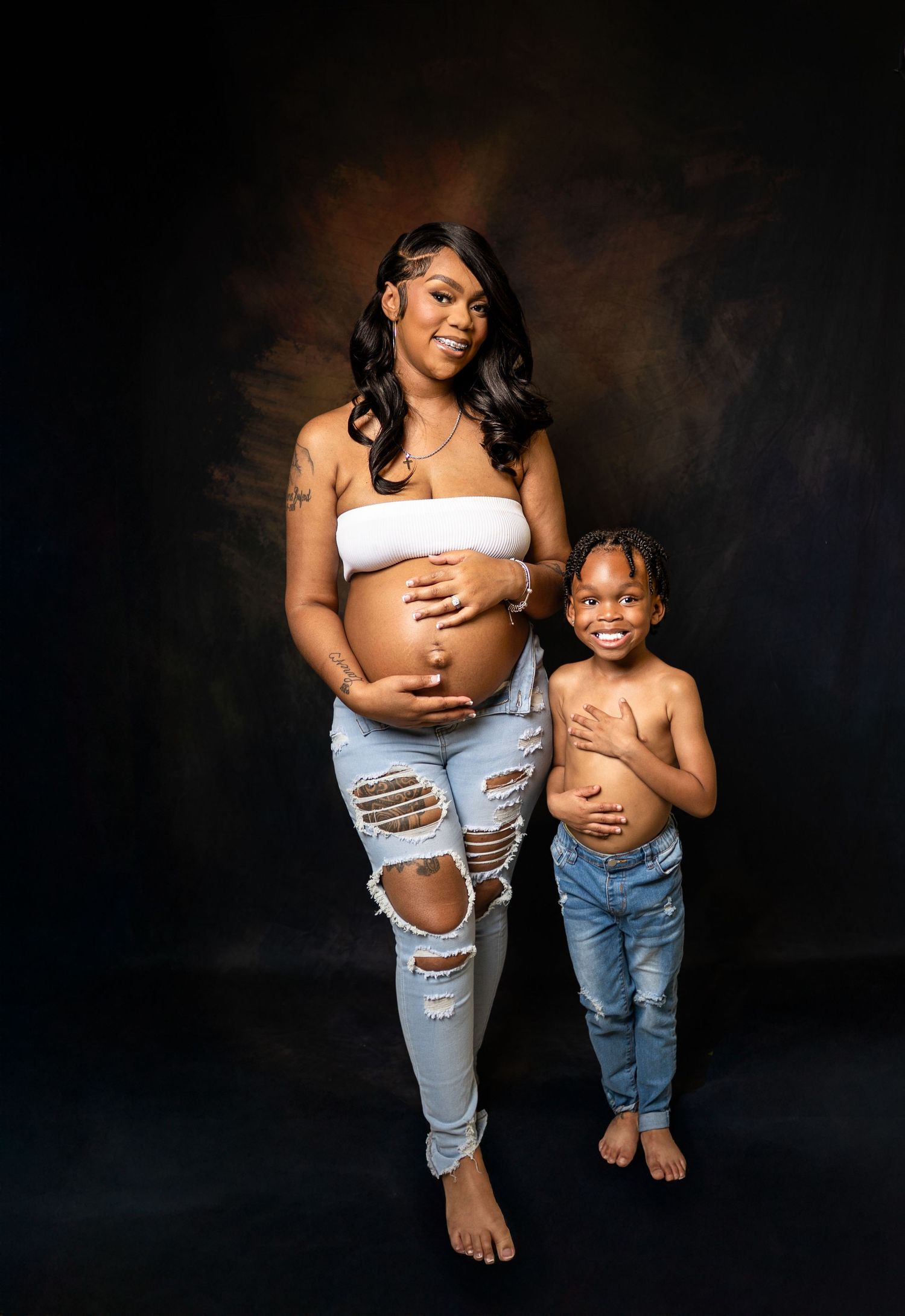 Pregnant woman and young child pose together in matching ripped jeans for a maternity photo shoot.