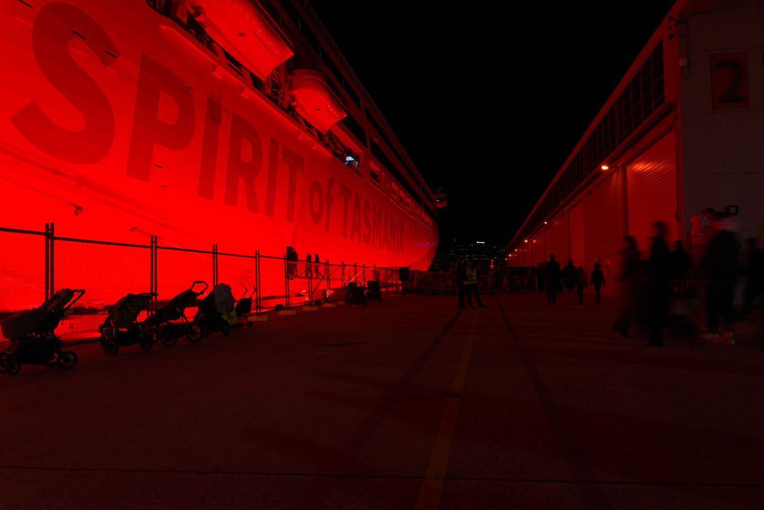 A building illuminated in vivid red light with SPIRIT text at night, silhouettes of people walking along the path.