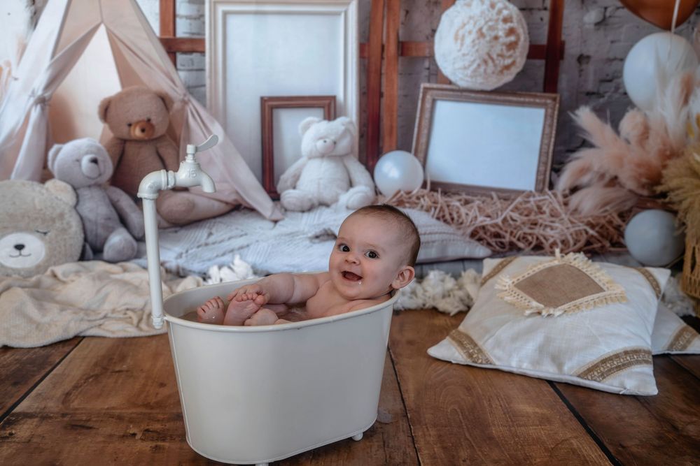 Un bébé souriant se détend dans une mini baignoire, sur un décor de studio photo