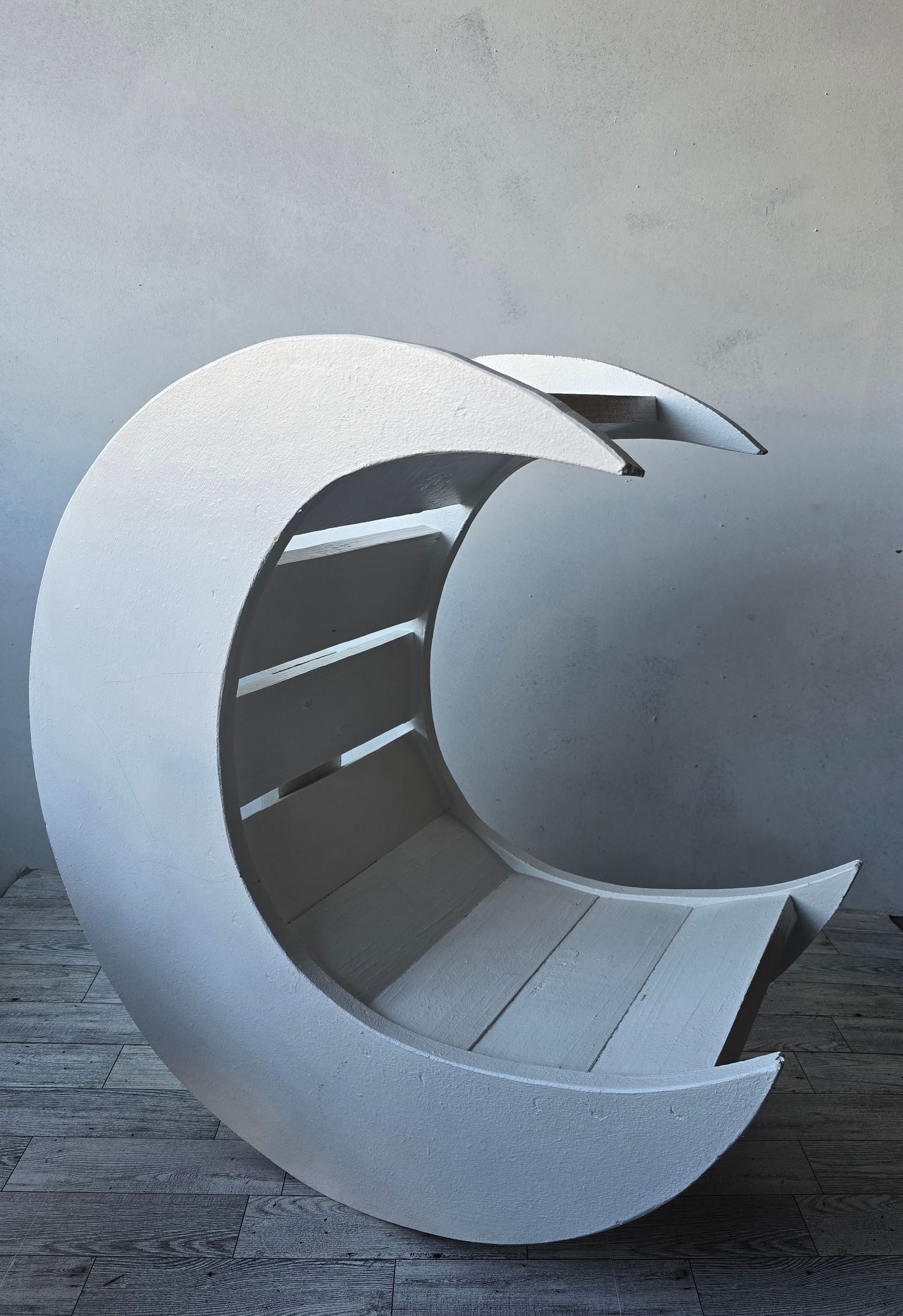 Modern crescent moon-shaped white bench with slatted seating, minimalist sculptural furniture design against gray wall.