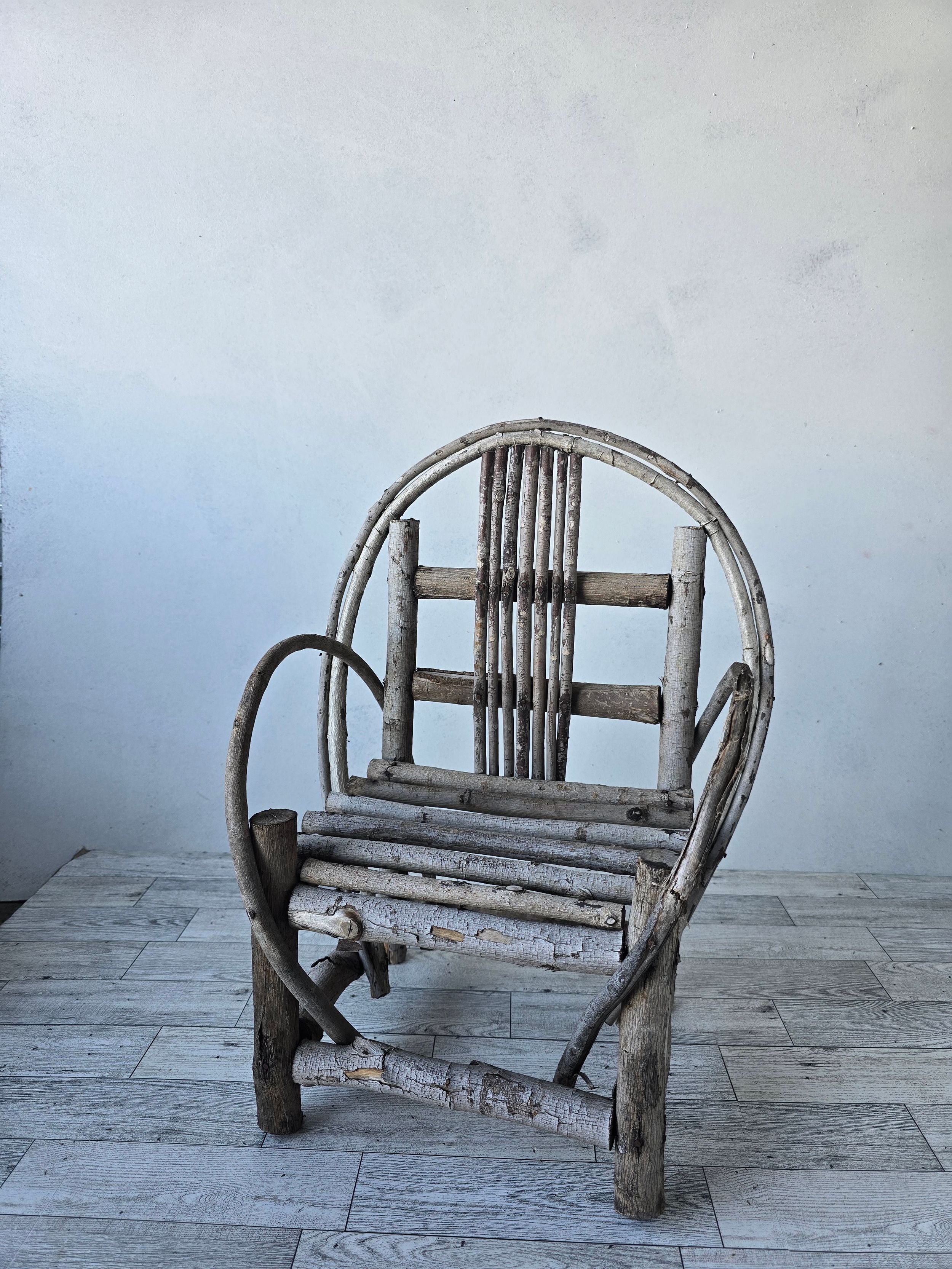 Rustic handmade twig branch armchair with circular back, natural wood construction, weathered finish, folk art style.