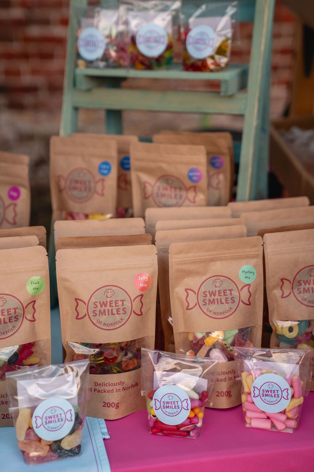 Sweet Smiles branded kraft paper candy bags displayed on a pink table at an outdoor market stall.