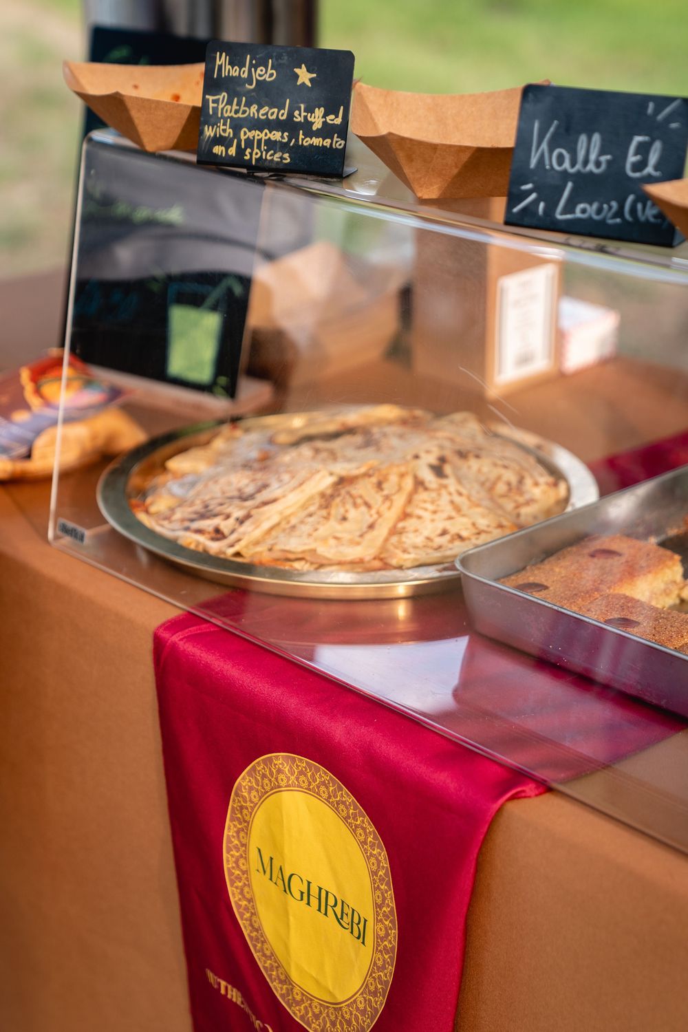 Maghrebi flatbread display case with Mudjeb stuffed flatbread on silver tray at a food stall.
