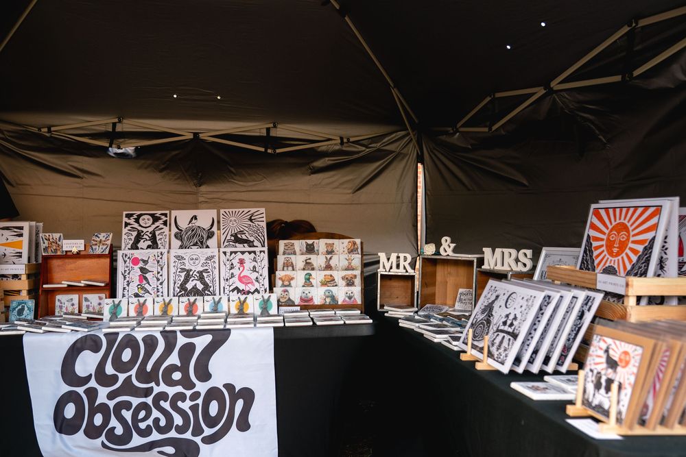 Cloud Obsession art vendor booth displaying colorful prints, framed artwork, and Mr & Mrs signs at an outdoor market event.