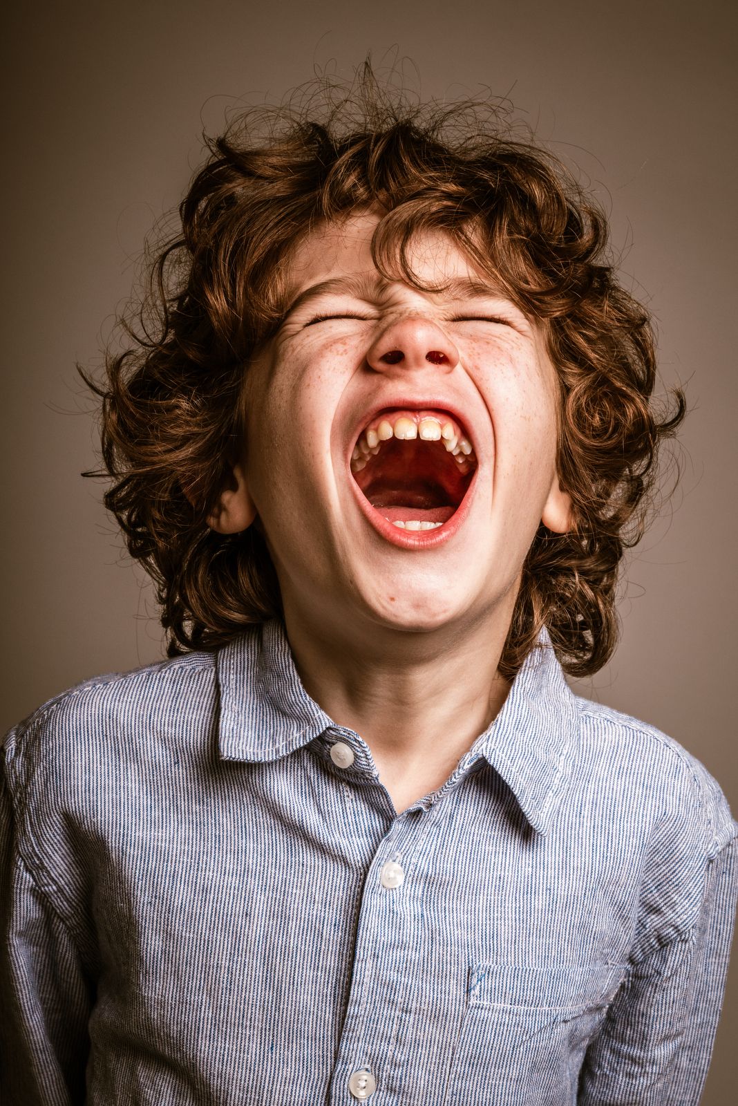 Expressief studioportret van een kind met krullend haar, gesloten ogen en de mond uitbundig open.