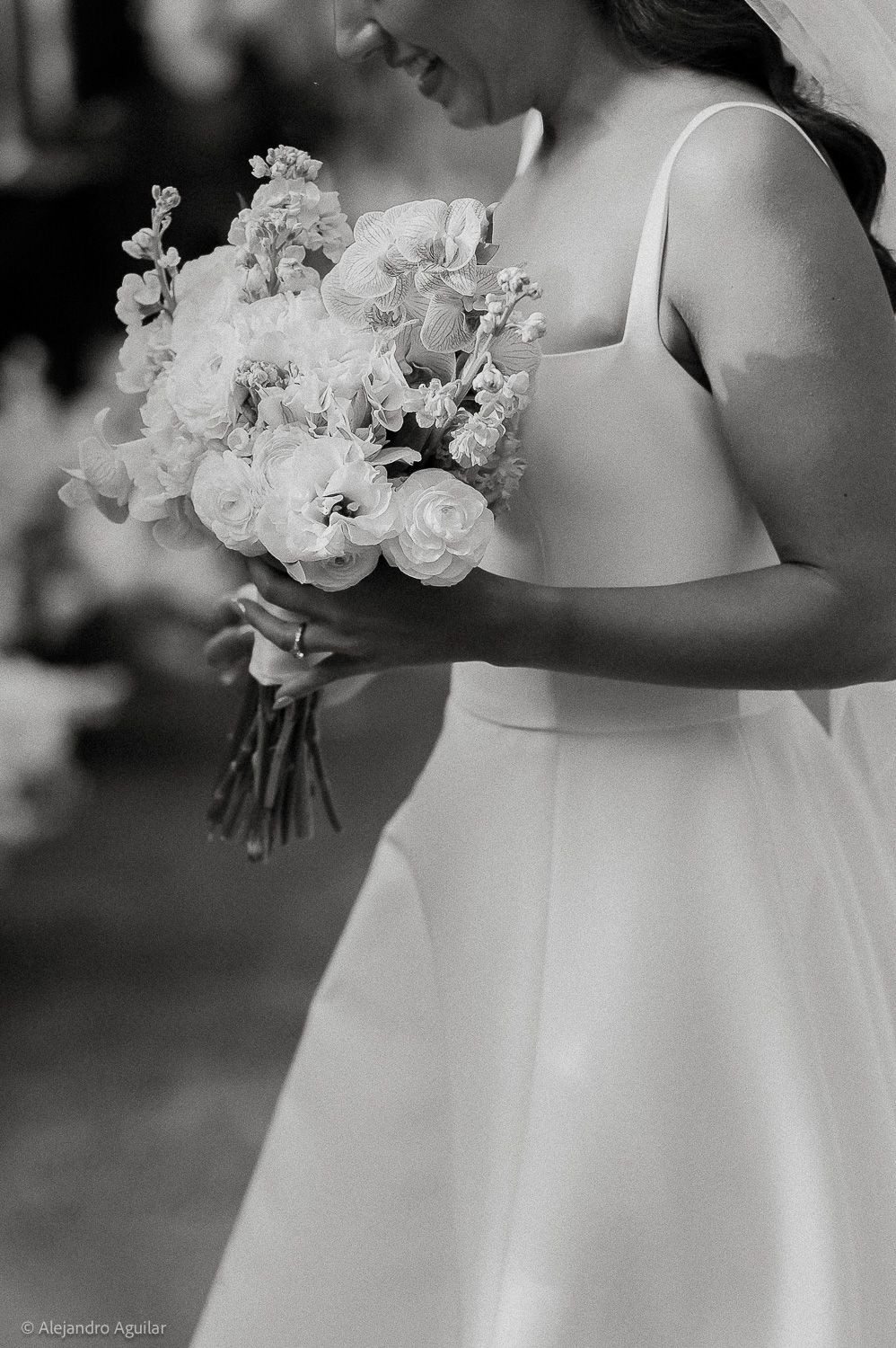 Bride in white dress holding elegant bouquet of roses and flowers, black and white wedding photography.