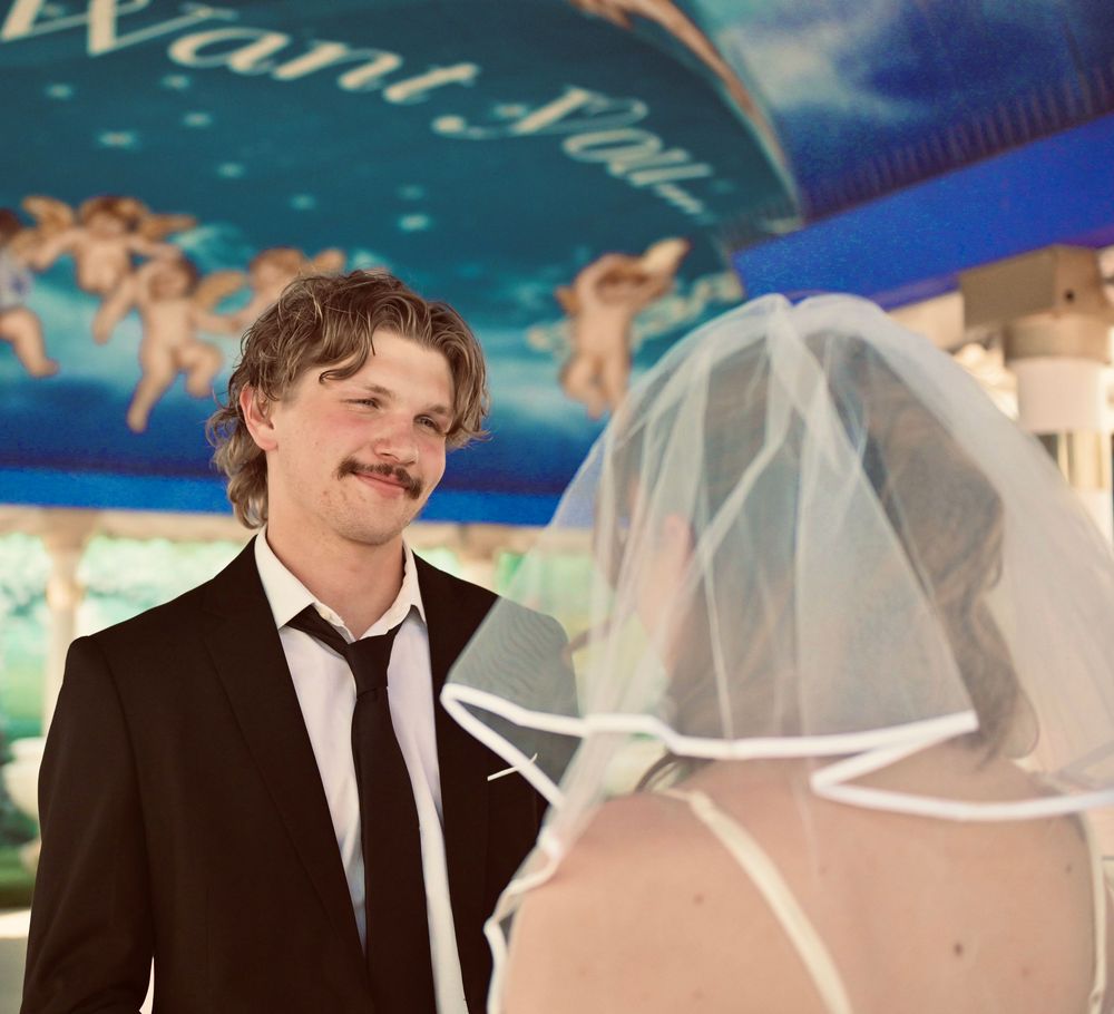 Groom in black suit smiling at bride in white veil at Las Vegas wedding chapel.