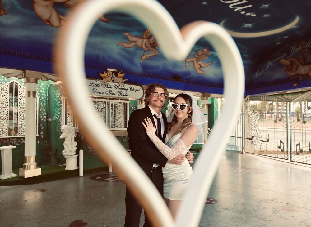 Couple posing romantically inside a heart-shaped frame at a Las Vegas wedding chapel with angel murals.