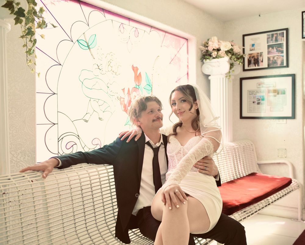 Newlywed couple posing on a white wicker bench inside a decorated Las Vegas wedding chapel.