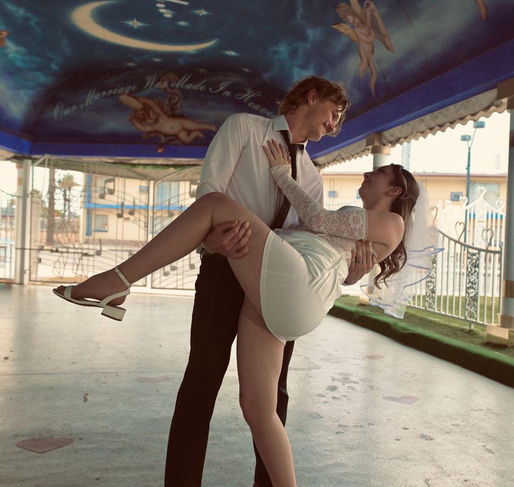 Groom lifts bride in a white mini dress under a painted ceiling at a Las Vegas wedding venue.