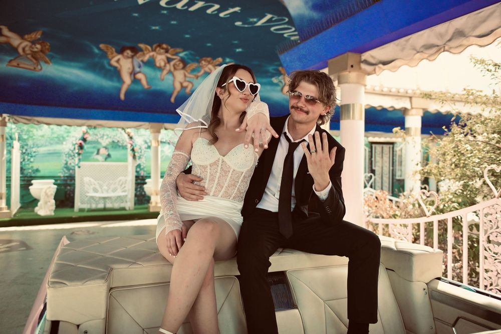 Couple in wedding attire posing on a white bench at a Las Vegas chapel tunnel of love attraction.
